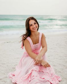 a woman in a pink dress is sitting on the beach and smiling at the camera