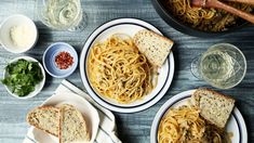 two plates with spaghetti and bread on them next to glasses of water, hotdog buns, and garlic bread