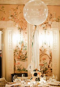 a dining room table is set with white plates and silverware, an oversized balloon hangs from the ceiling