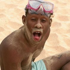 a man with goggles on his head is sitting in the sand and has his mouth open