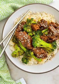 beef and broccoli over rice in a bowl with chopsticks on the side