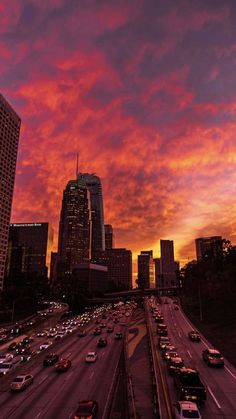 the sun is setting over a city with tall buildings and cars driving down the road