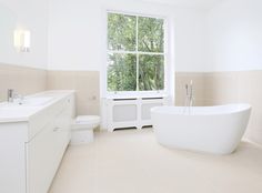 a white bath tub sitting under a window next to a toilet and sink in a bathroom