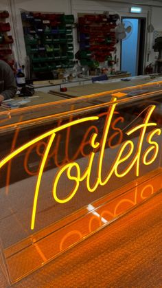 a neon sign that says toilets on it in front of a desk with two men working behind it