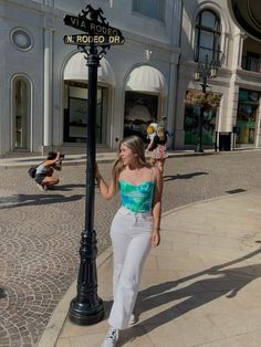 a woman standing next to a street sign on a pole in front of a building