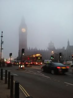 cars driving down a street in front of a clock tower on a foggy day