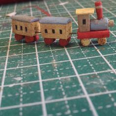 two small wooden toy trains sitting on top of a green table next to a red bag