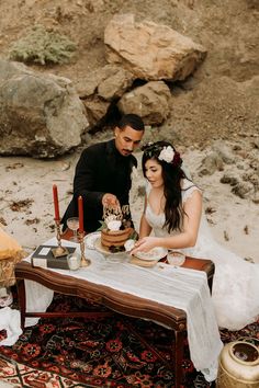 a bride and groom cutting their wedding cake at the table in front of some rocks