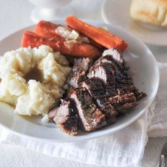 a white plate topped with meat, mashed potatoes and carrots next to bread