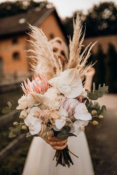 a woman in a white dress holding a bouquet of flowers and feathers on her wedding day