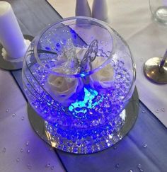 a table topped with a glass bowl filled with purple flowers and white roses next to candles