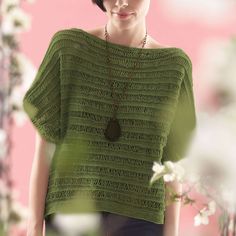 a woman standing in front of a pink wall wearing a green knitted sweater and necklace