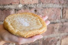 a person holding a cookie in front of a brick wall with white powder on it