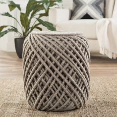 a woven stool sitting on top of a rug next to a white couch and potted plant