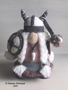 a crocheted stuffed animal wearing a helmet and holding two swords