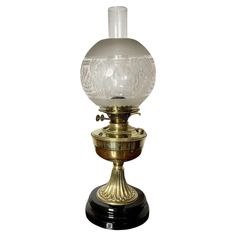 an old fashioned glass and brass lamp on a black stand with a white light behind it