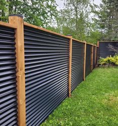 a wooden fence in the grass next to a black metal wall and some green trees