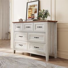 a white dresser sitting in a room next to a painting on top of a wall