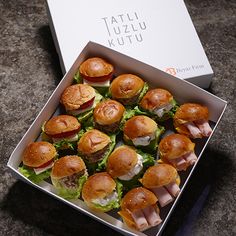 a box filled with mini sandwiches sitting on top of a stone counter next to a white box