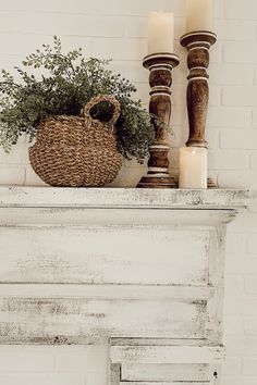 an old fireplace mantel with candles and a basket filled with greenery on top