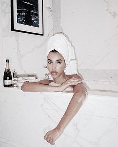 a woman sitting in a bathtub with a towel on her head and a bottle next to her