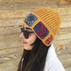 a woman wearing sunglasses and a crocheted beanie is standing in front of a wooden wall