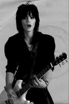 a woman with black hair playing an electric guitar in front of a white background,