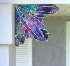 a stained glass window hanging from the side of a white building with an artistic design on it