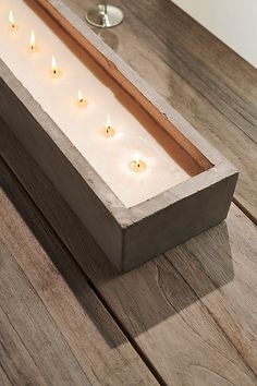 several candles are lit in a wooden box on the table next to a wine glass