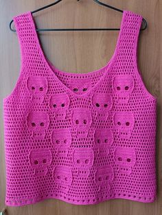 a pink crocheted top hanging on a wooden wall