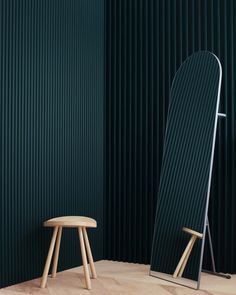 a wooden stool sitting next to a large mirror in a room with green walls and vertical blinds