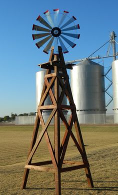 a wooden windmill sits in the middle of a field with two silos behind it