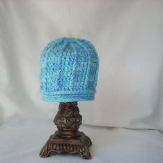 a blue knitted hat sitting on top of a wooden stand in front of a white background