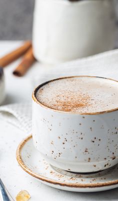 there is a cup and saucer on the table with cinnamon sticks in the background