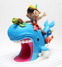 a figurine of a boy riding on top of a blue whale with its mouth open