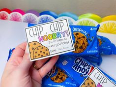 a person holding up some chips chip hooray cookies in front of colorful balloons