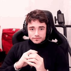 a man wearing headphones sitting in front of a computer desk with red bags behind him