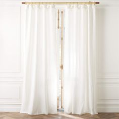 a white curtain with gold trim hanging in front of a wooden floor and wall behind it