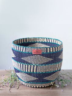 a blue and white woven basket sitting on top of a wooden table next to flowers