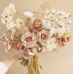 a person holding a bouquet of flowers in front of a beige wall with white and pink flowers