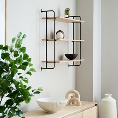 a wooden table topped with a bowl next to a shelf filled with vases and bowls