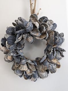 a wreath made out of seashells hanging on a rope with a white wall in the background