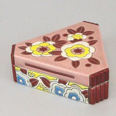 a small pink box with flowers painted on the top and bottom, sitting on a white surface