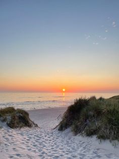 the sun is setting over the ocean and sand dunes in front of an empty beach