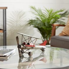 a toy airplane sitting on top of a glass table next to a chair and potted plant