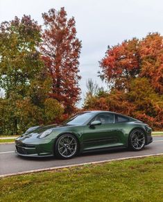 a green sports car driving down the road in front of trees with orange and red leaves