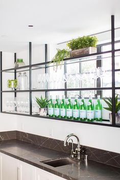 a kitchen sink under a mirror filled with green bottles