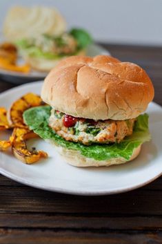 a chicken sandwich with lettuce and tomatoes on a white plate next to chips