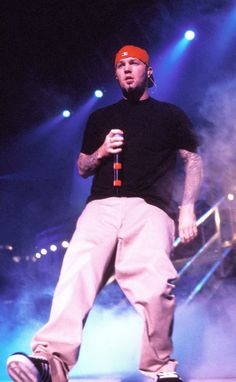 a man standing on stage holding a microphone in his right hand and wearing an orange hat