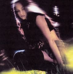 a woman sitting in the grass with her legs spread out and lights shining behind her